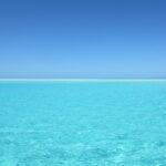 A calm clear blue ocean, beach in the distance.