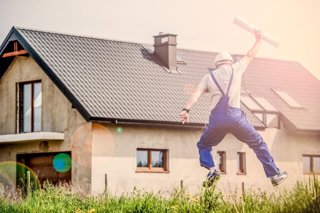 Architect with blueprint jumping for joy in front of a house.