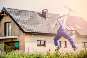 Architect with blueprint jumping for joy in front of a house.