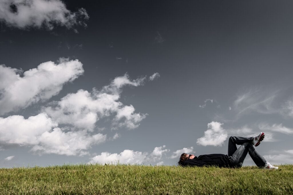 Man lying on the grass, daydreaming and thinking under open sky.