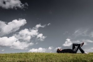 Man lying on the grass, daydreaming and thinking under open sky.