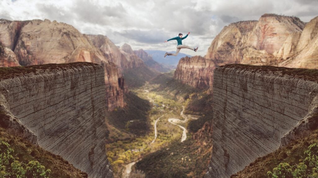 A man jumping over an impossibly large canyon with river below.