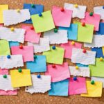 A bulletin board with a variety of white and colored blank scraps of paper on it.
