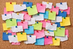 A bulletin board with a variety of white and colored blank scraps of paper on it.