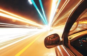 A car heading fast down the street, from the driver perspective, with light beams streaming outward towards the highway.