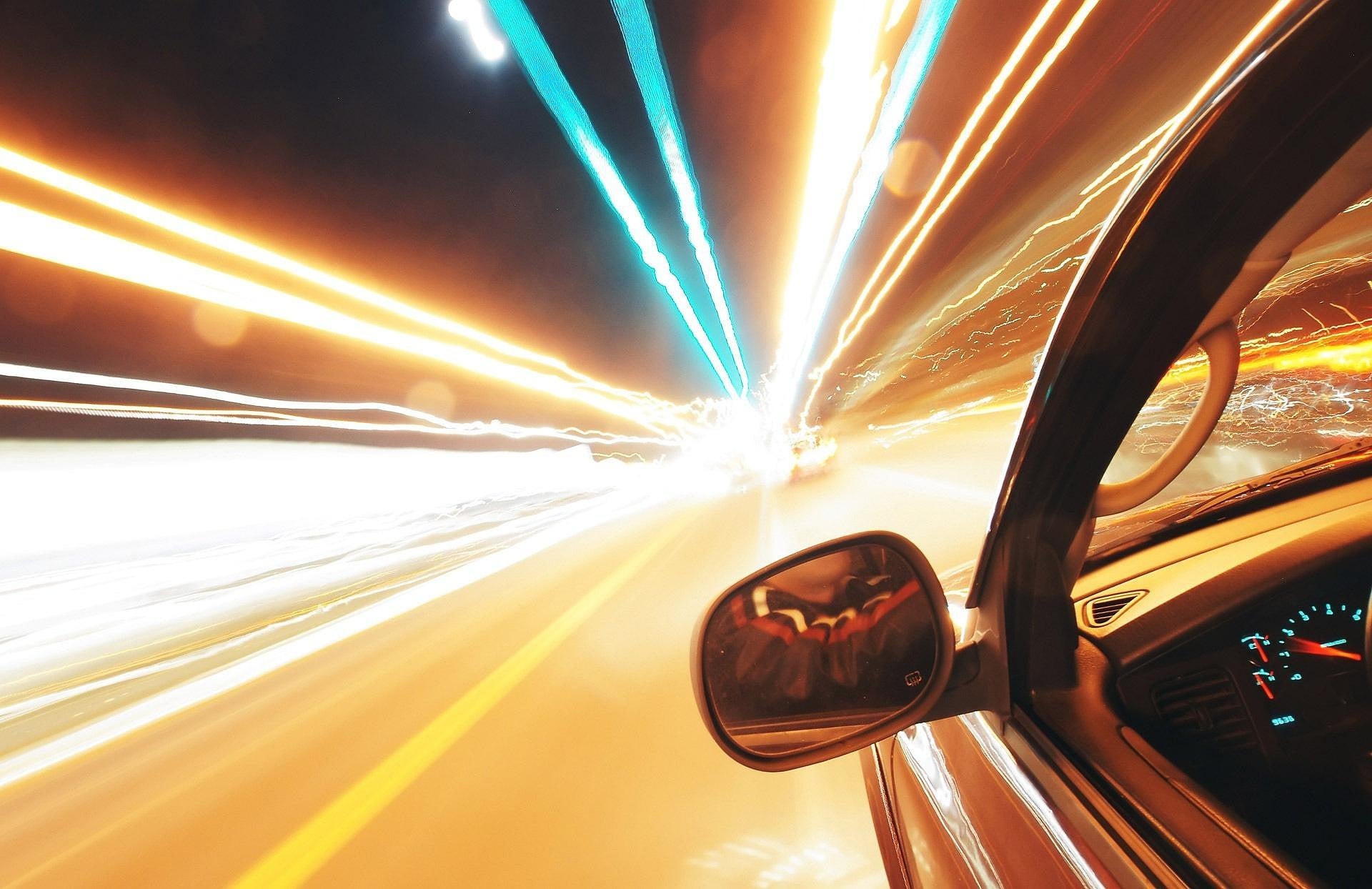 A car heading fast down the street, from the driver perspective, with light beams streaming outward towards the highway.