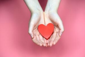 Open hands holding a wooden red heart.