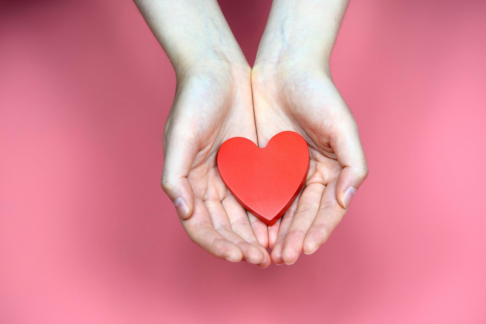 Open hands holding a wooden red heart.
