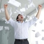 Businessman celebrating in the office, throwing a variety of papers up in the air.
