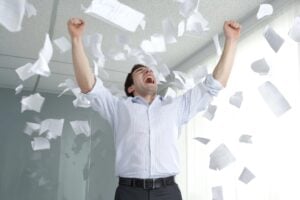 Businessman celebrating in the office, throwing a variety of papers up in the air.