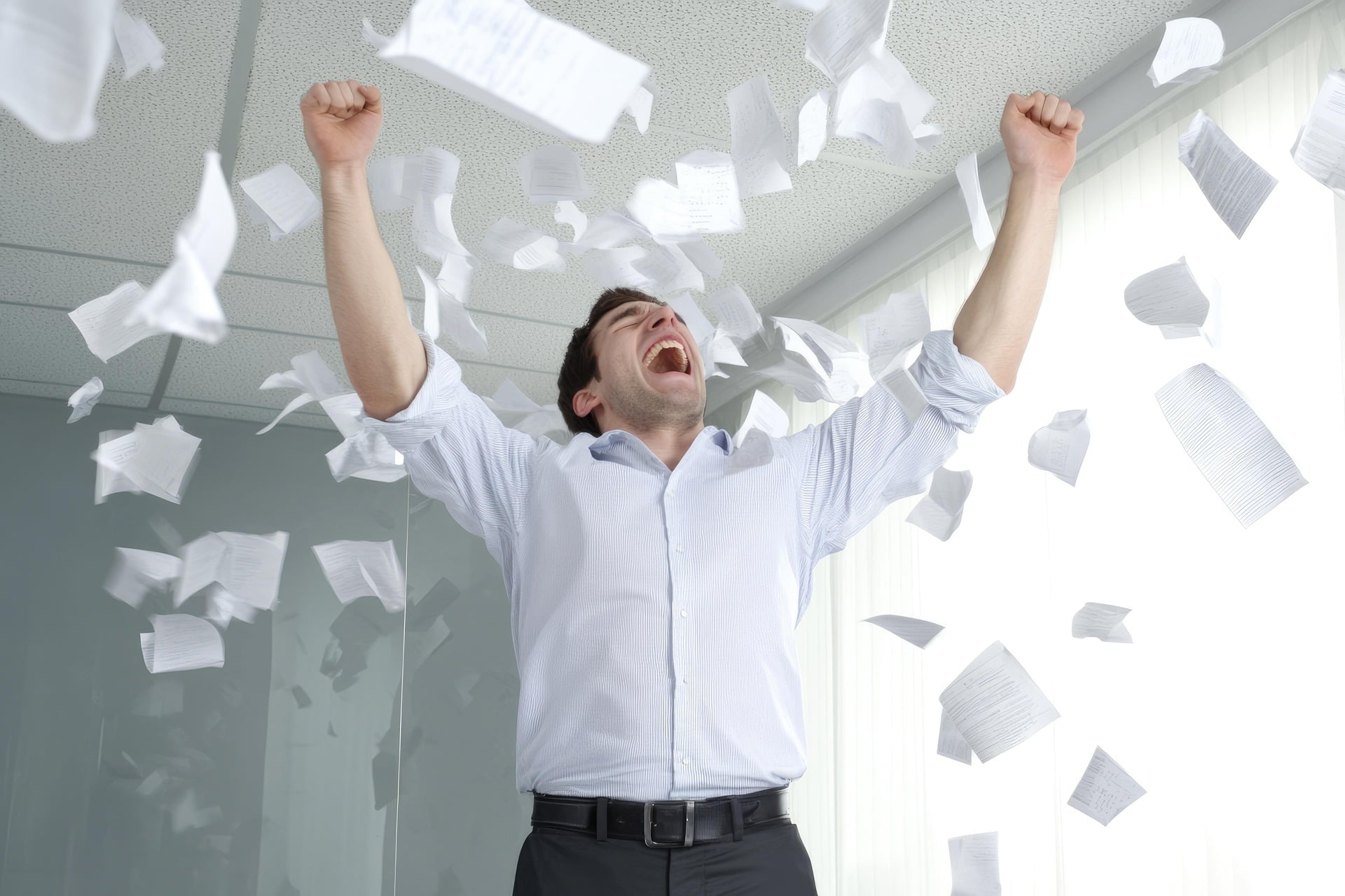 Businessman celebrating in the office, throwing a variety of papers up in the air.