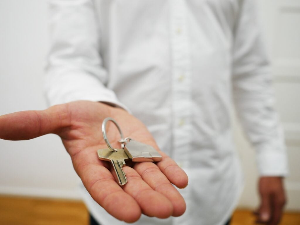 A person in background holding out a key in outstretched hand.