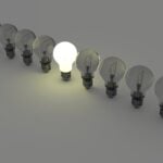 A row of light bulbs, all dark, except one shining bright in the center.
