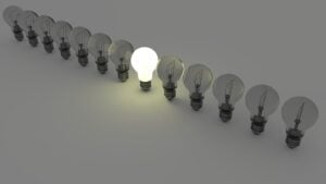 A row of light bulbs, all dark, except one shining bright in the center.
