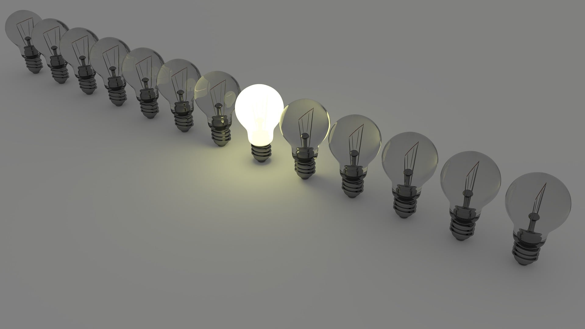 A row of light bulbs, all dark, except one shining bright in the center.